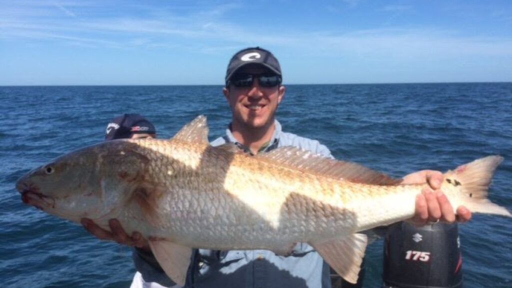Happy angler standing on back of Pipe Dream Charters III holding a Redfish caught at Amelia Island