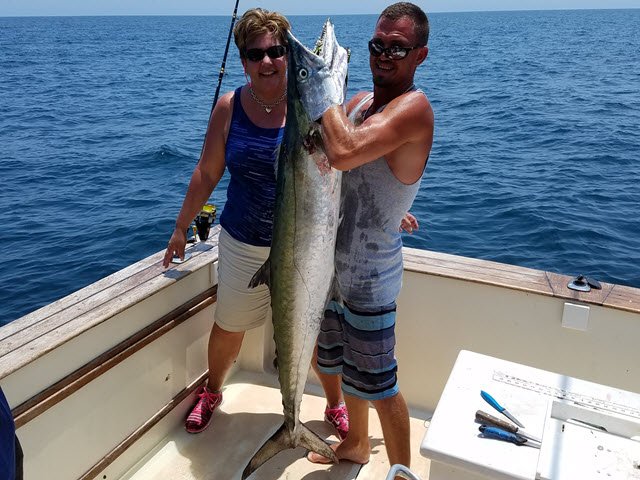 Kingfish fishing charters Amelia Island: an angler holding a king mackerel on the deck of Pipe Dream III on the summer drift lanes off Amelia Island, Florida, on a Pipe Dream Charters private offshore trip from Fernandina Harbor Marina